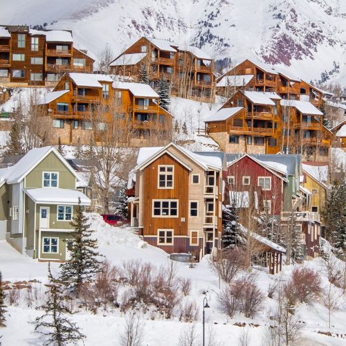Snow-covered hotels sit upon a steep hill with large mountains in the background, in the town of Mt. Crested Butte, Colorado.